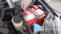 Автомеханик откручивает гаечным ключом минусовую клемму аккумулятора в подкапотном пространстве